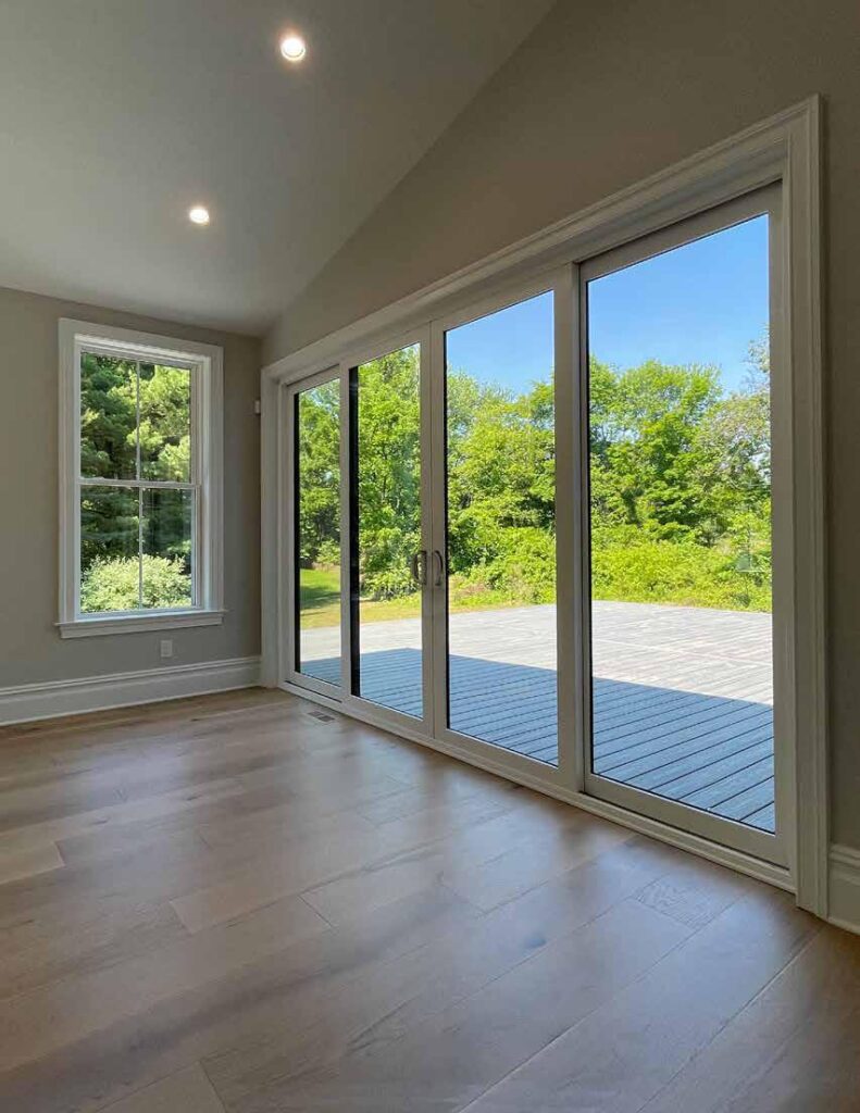 Four-panel OKNA Panorama sliding patio door with white frame and large glass panels overlooking a backyard deck