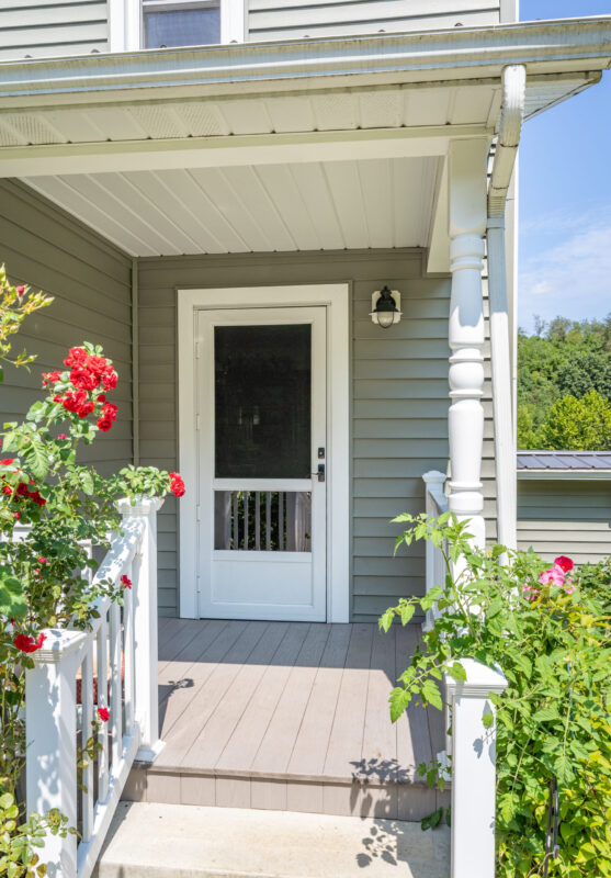 White ProVia Spectrum storm door with full-view screen and black hardware on a covered front porch with flowers