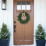 ProVia Signet fiberglass entry door with wood-grain finish, shown in a light Cleveland winter setting with snow-dusted evergreens.