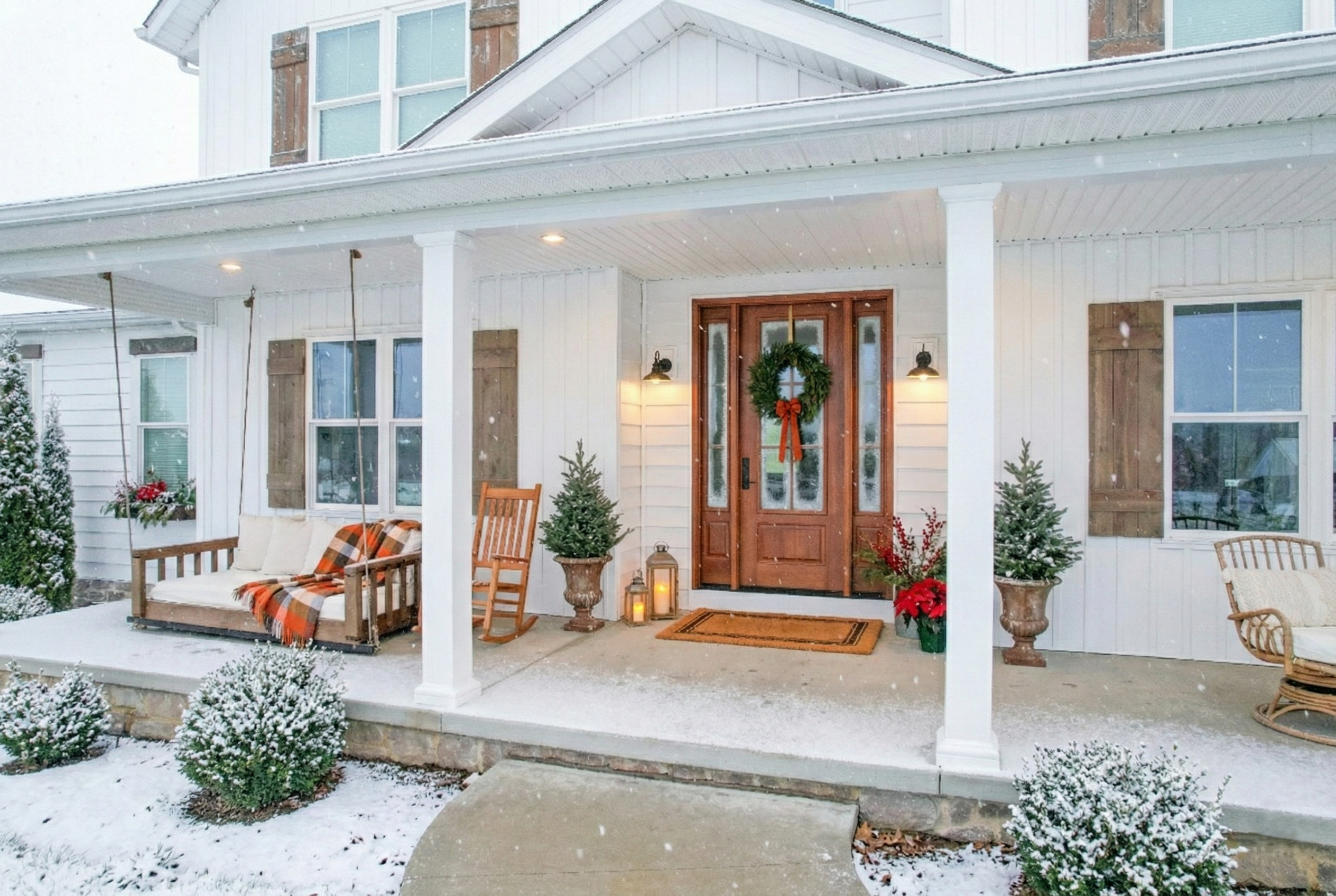 Winter front porch with a ProVia Signet Cherry entry door, seasonal decor, light snowfall, and a cozy blanket on the porch swing.