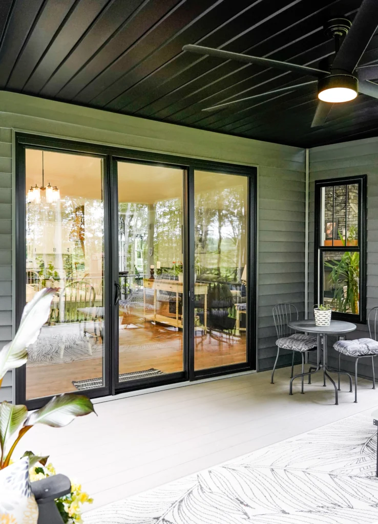 Modern black sliding patio door opening to a covered patio, featuring large glass panels and a contemporary exterior design.