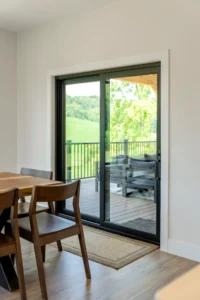 Modern black sliding patio door connecting a dining area to a covered deck with expansive views and natural light.
