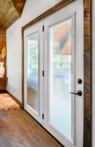White hinged patio door with integrated blinds between the glass and rustic wood trim in a modern home interior.